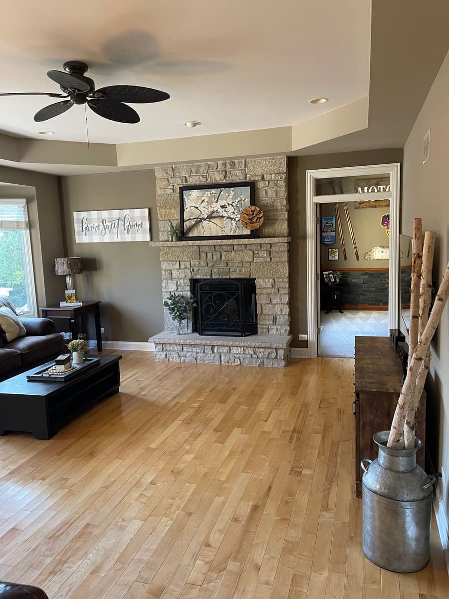 Furnished living room with a stone fireplace and hardwood floor catching light after standard house cleaning
